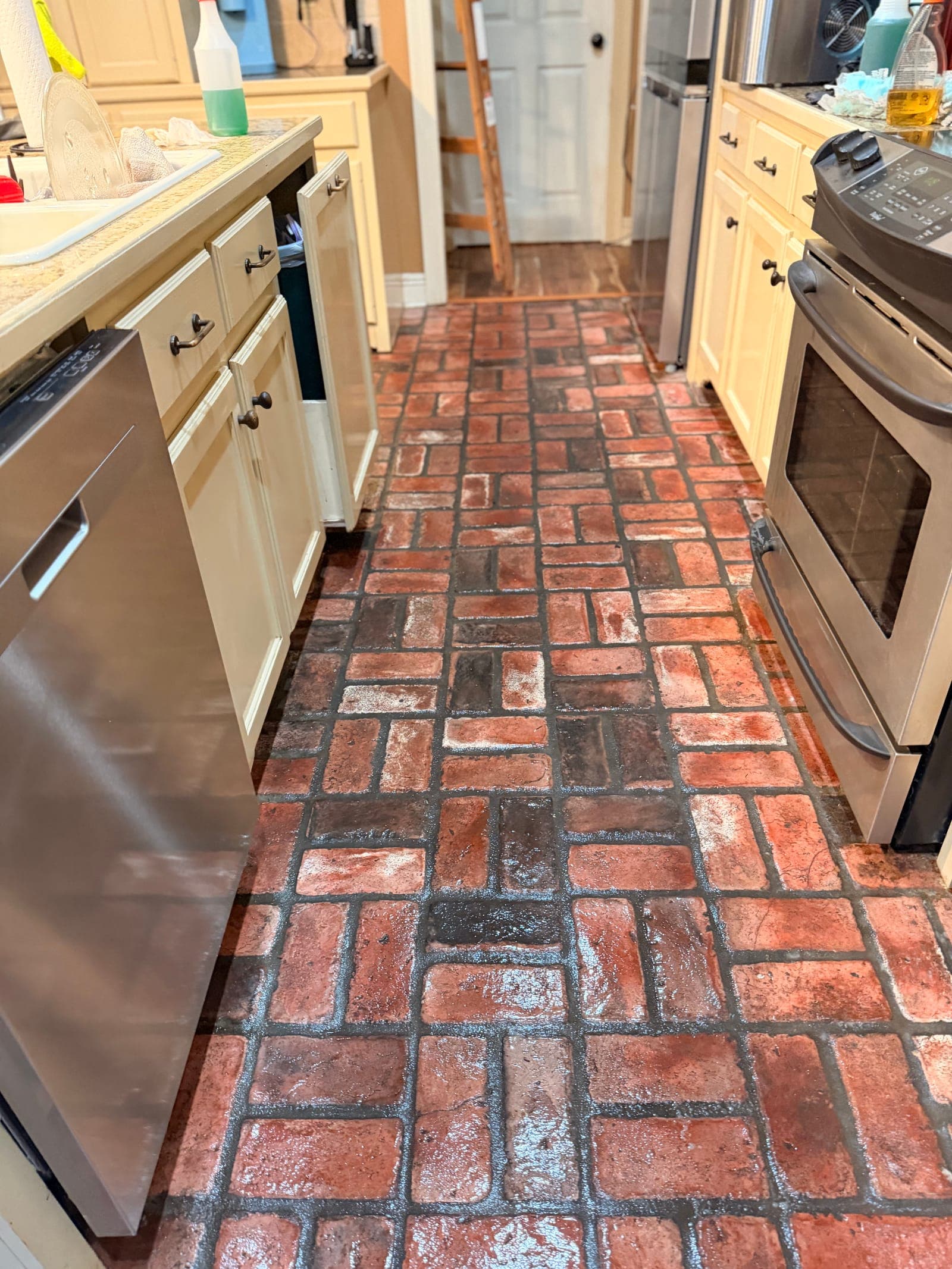 Freshly mopped brick-pattern kitchen floor between stainless appliances and cream cabinets
