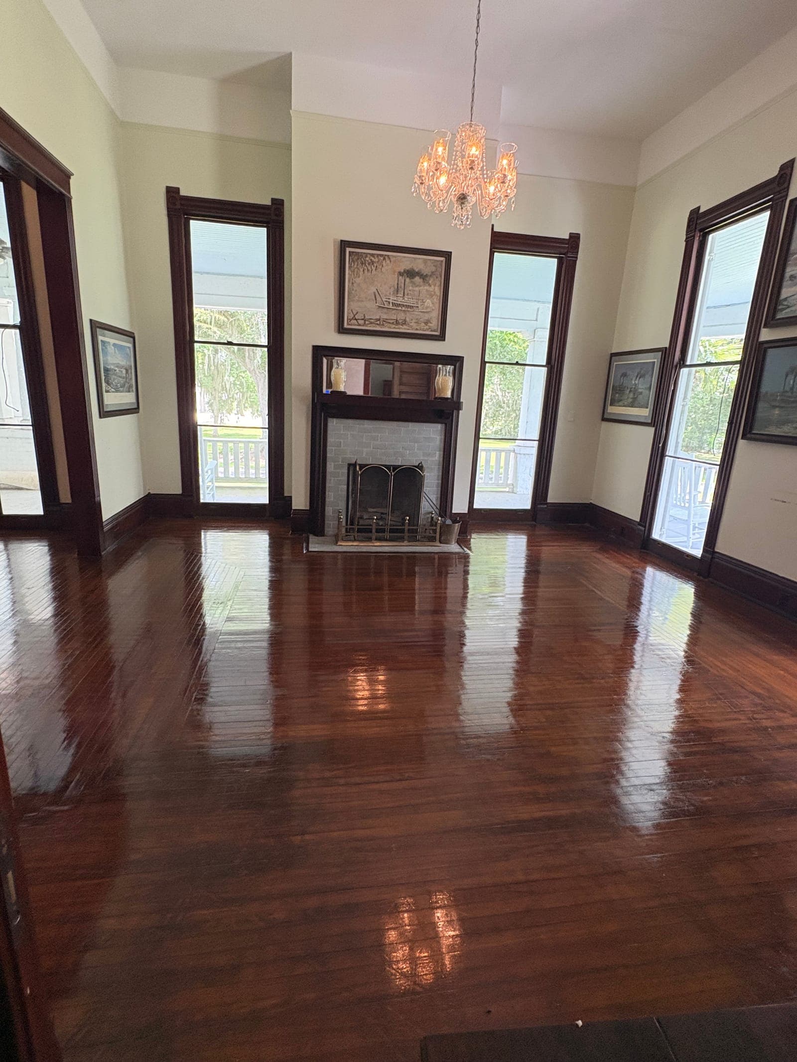 Freshly polished hardwood floor in a parlor with a fireplace, chandelier, and tall windows