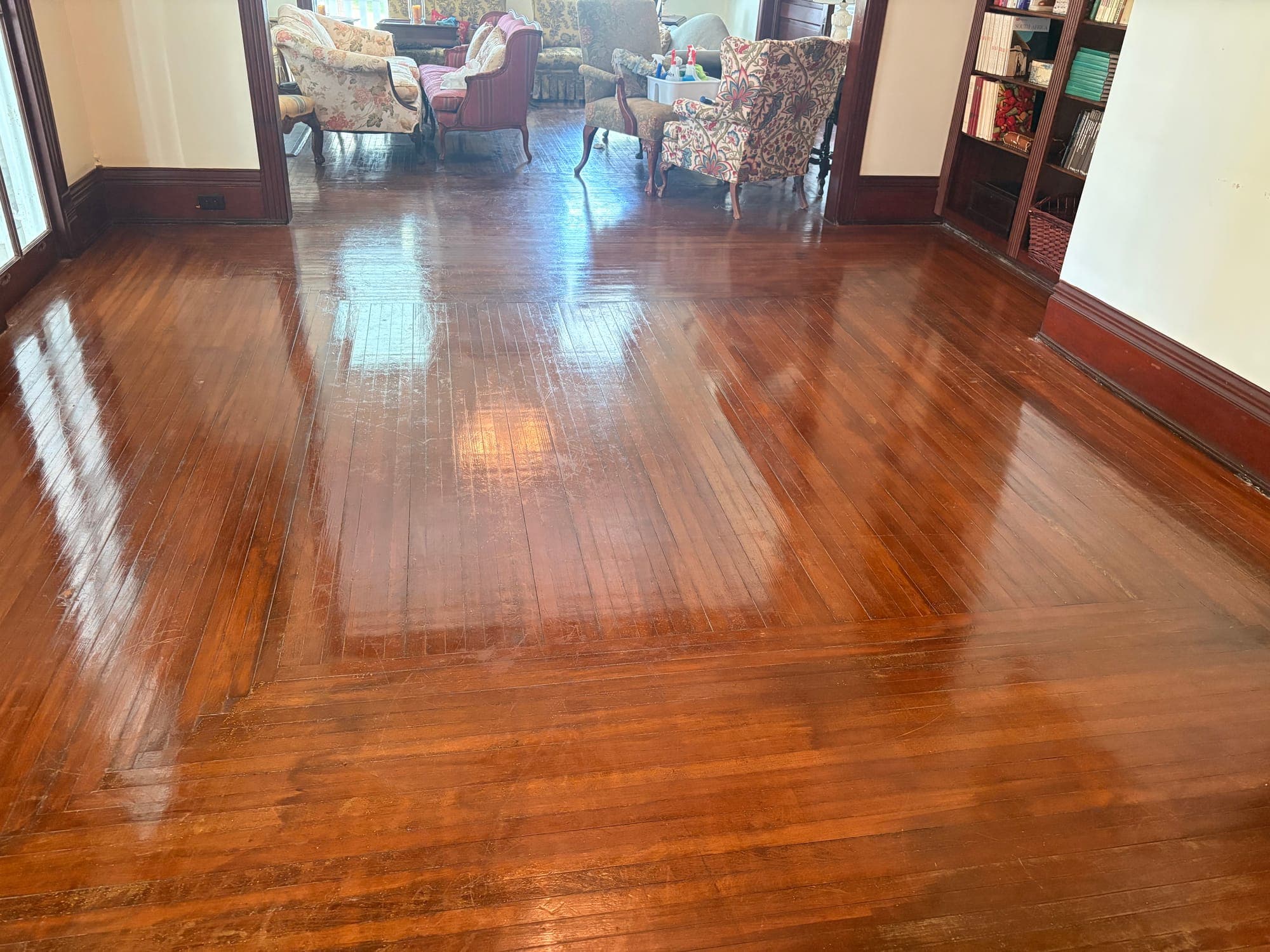 Polished hardwood floor reflecting light, with upholstered chairs and a bookcase beyond